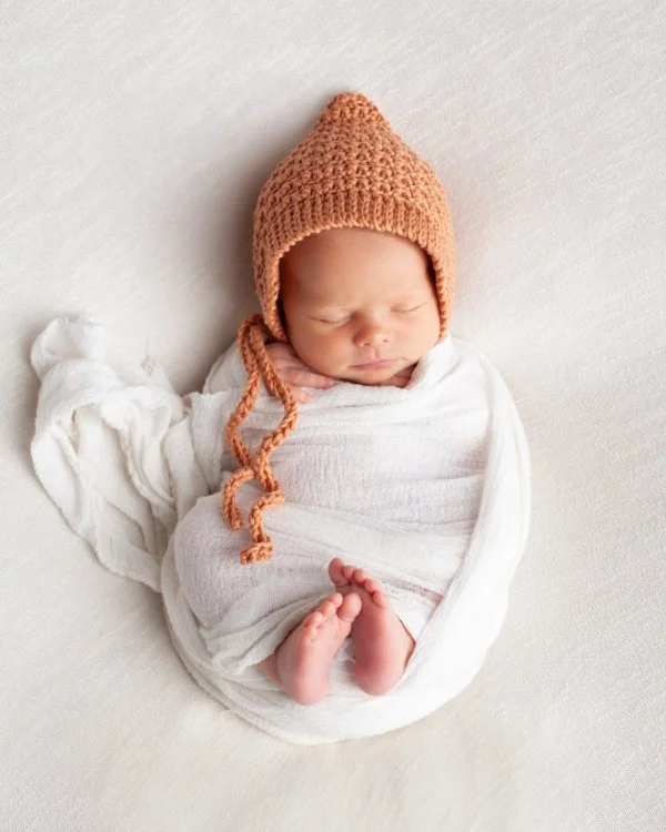 A newborn baby wearing a crochet bonnet.