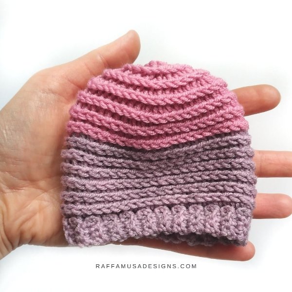 A tiny crochet preemie hat in the palm of a hand.