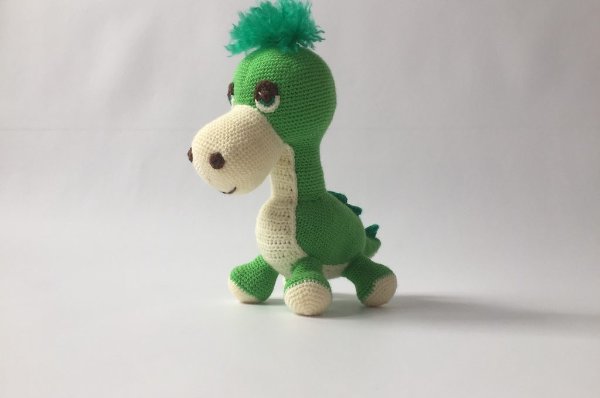 A green amigurumi crochet dinosaur with fluffy hair.