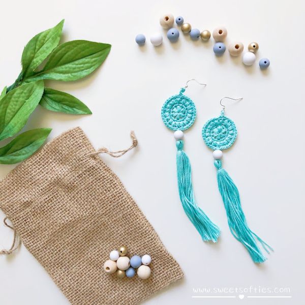A flat lay image of some beds, a little gift bag, and blue crochet earrings with long tassels.