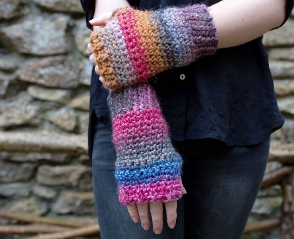 A woman wearing long fingerless gloves crocheted in self-striping yarn.