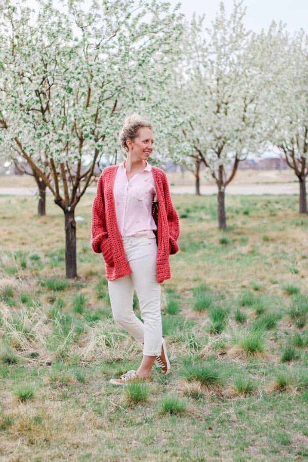 A woman in a garden wearing a red coloured crochet hexagon cardigan with pockets.