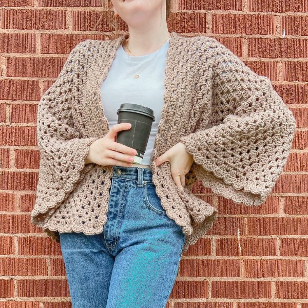 A woman wearing a cropped crochet hexagon cardigan with oversized sleeves.