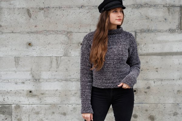 A woman wearing a grey crochet cropped sweater with black jeans.