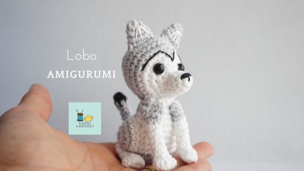 A small amigurumi wolf sitting in the palm of a hand.