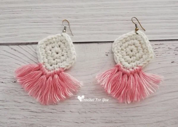 White diamond-shaped crochet earrings with pink tassels.
