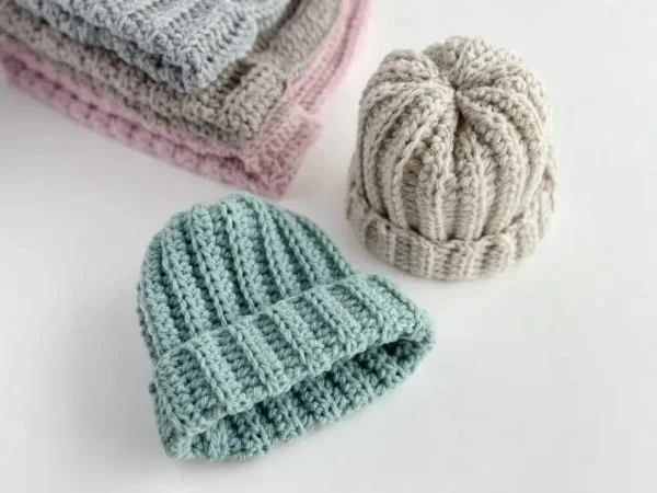 Two different coloured newborn crochet hats with fold up brims.