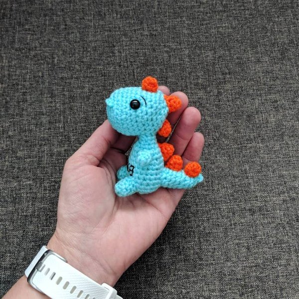 Someone holding a mini crochet t-rex dinosaur in the palm of their hand.