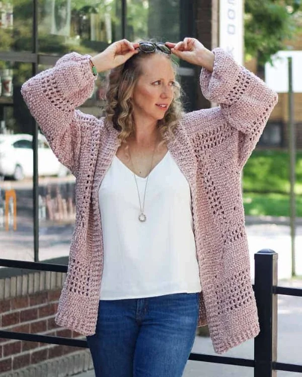 Woman waearing a pink crochet hexagon cardigan with jeans and a white top.