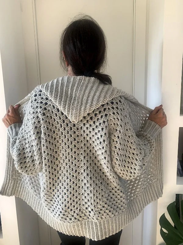 Back view of a woman wearing a grey crochet hexagon cardigan with a hood.