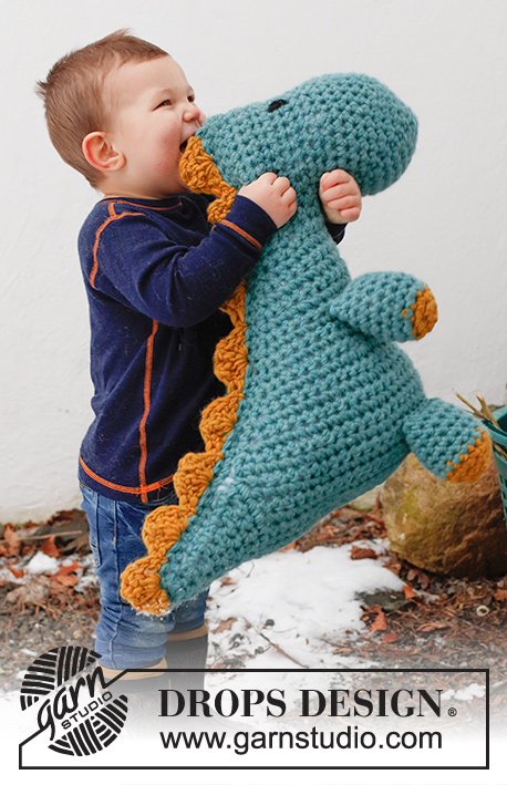 A child cuddling a large crochet dinosaur.