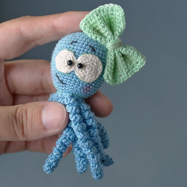 A cute crochet octopus with a funny expression, long tentacles, and a big green bow on her head.