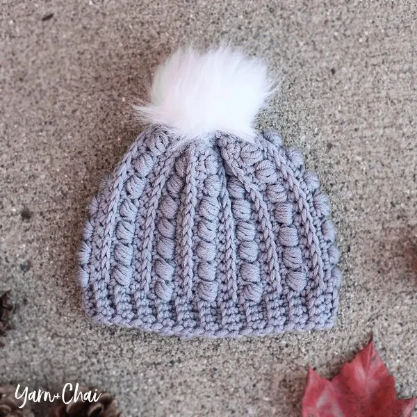 A crochet newborn baby hat with a fur pompom.