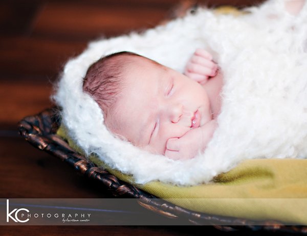 A closeup of a newborn baby sleeping in a fluffy white crochet baby cocoon.