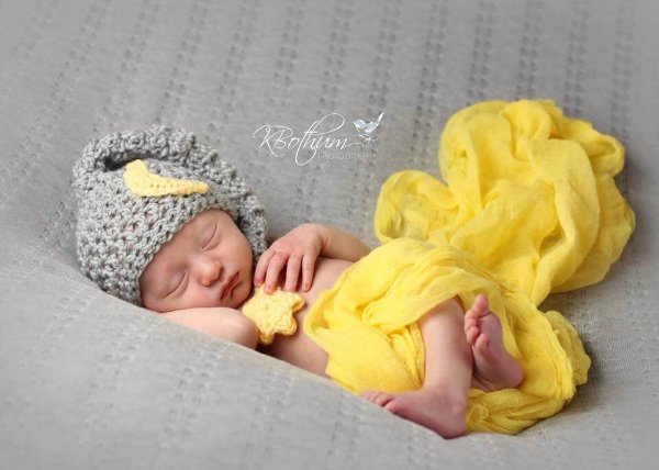 A newborn baby wearing a grey crochet what with a crescent moon motif.