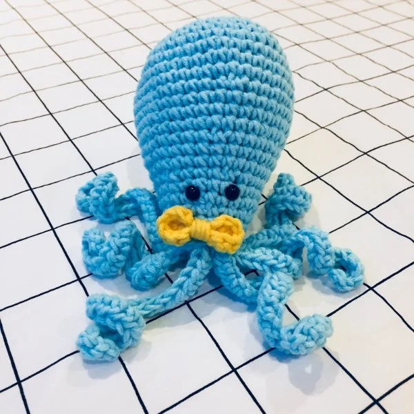 A cute blue crochet octopus with a yellow bow tie.