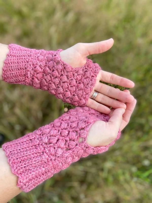 A woman wearing pink fingerless crochet mittens.