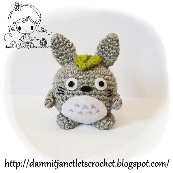 A small, round plush Totoro amigurumi with a leaf on it's head.