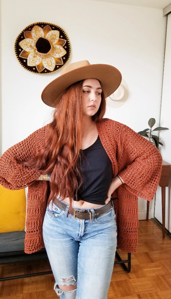 A woman wearing a rust coloured crochet hexagon duster cardigan.