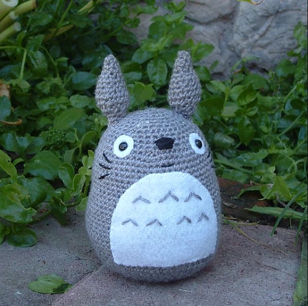 A crochet totoro sitting in on a garden path.