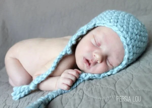 A newborn baby wearing a crochet hat with earflaps.