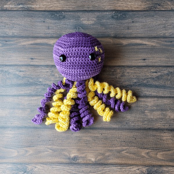 A purple and yellow crochet octopus with curly tentacles.