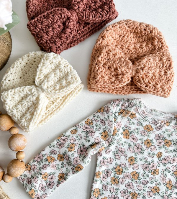 A flat lay image of a baby suit and three crochet newborn baby hats in different colours.