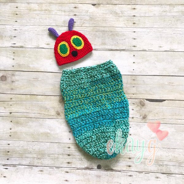 A flat lay image of a Very Hungry Caterpillar themed crochet baby cocoon and hat.