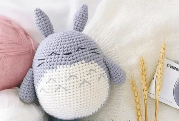 A chubby crochet totoro toy on a bed.
