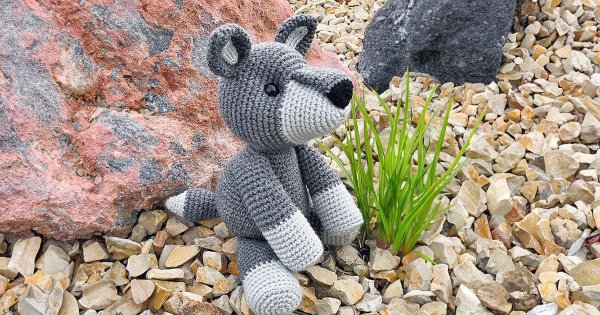 A large crochet wolf toy sitting in a garden.