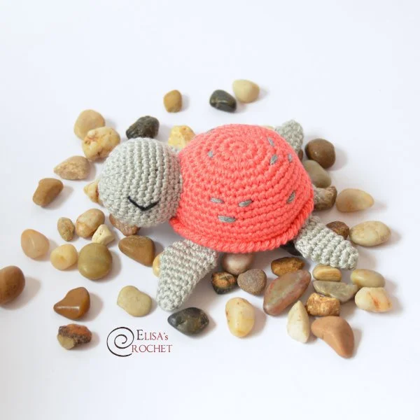A cute crochet turtle sitting on a pile of pebbles.