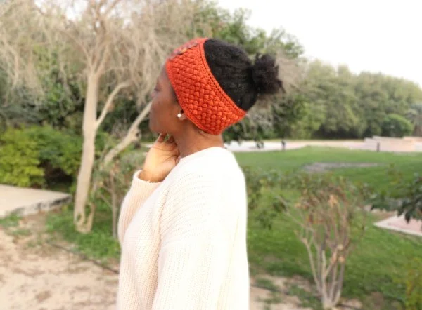 A woman wearing a brightly coloured crochet earwarmer with buttons.