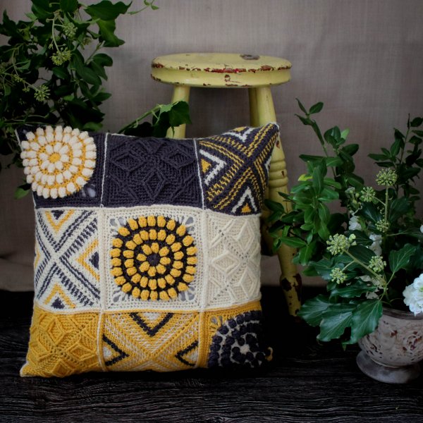 A large granny square pillow in shades of black, yellow, grey, and white.