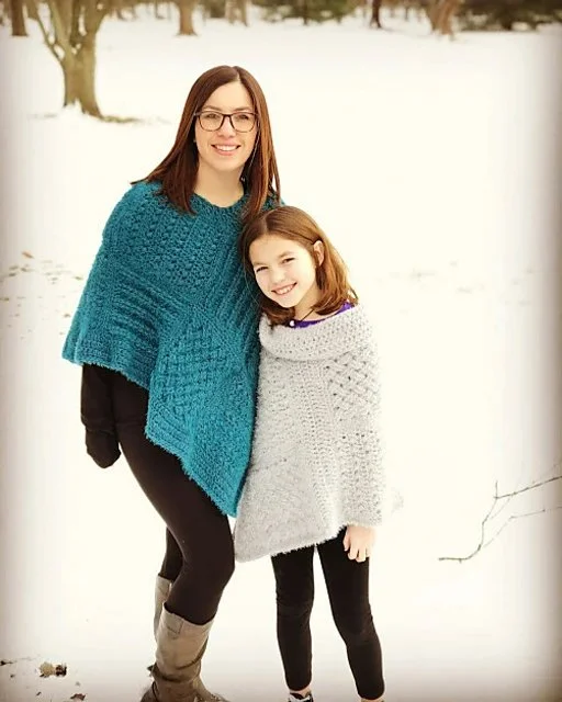 A woman and a child wearing matching crochet ponchos.