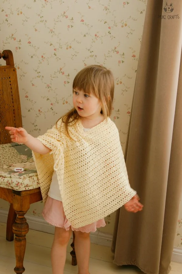 A young child wearing a cream coloured crochet poncho.