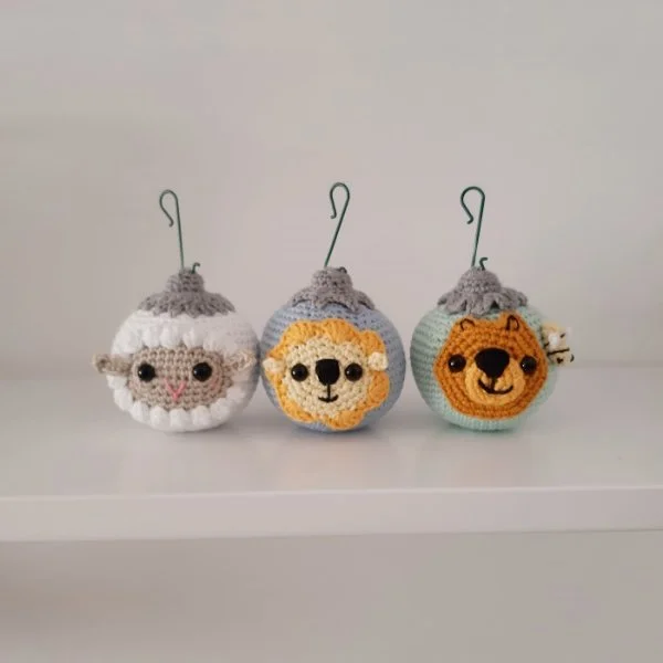 Three different animal-themed crochet christmas baubles - a sheep, a lion, and a bear.
