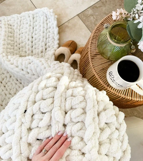 A close-up image of a chunky crochet blanket on a woman's lap