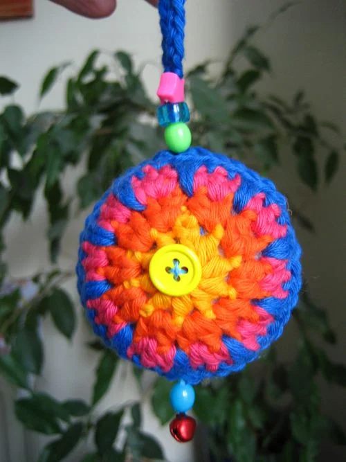 A brightly coloured crochet bauble decoration with beads and a bell embellishment.