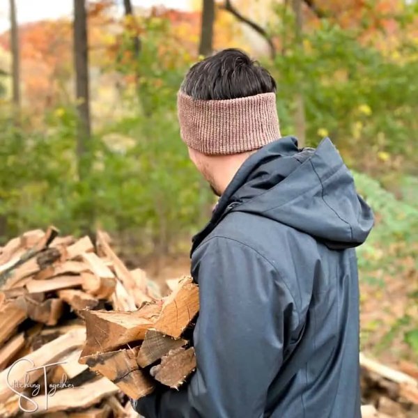 A man wearing a crochet earwearmer and carrying firewood