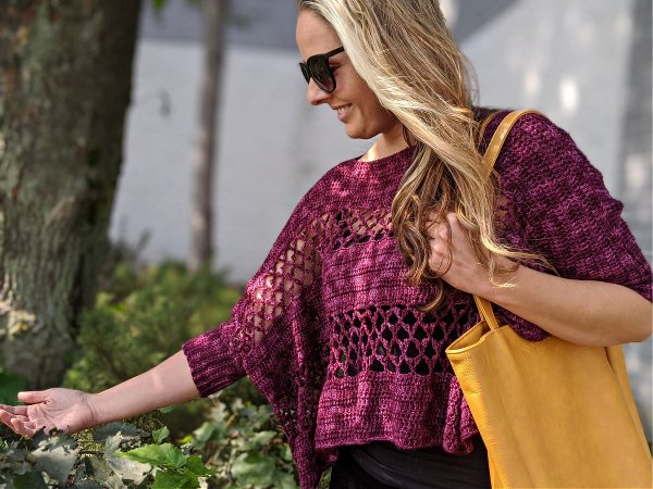 A woman wearing a cropped crochet pullover woth a lacy stitch pattern.