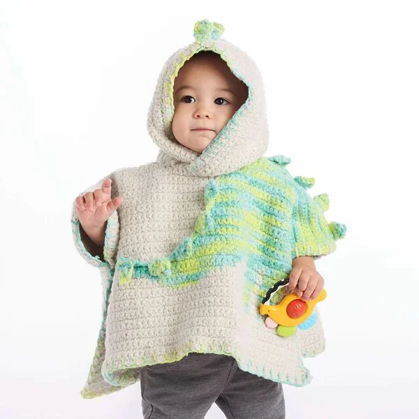 A toddler wearing a crochet poncho with a dinosaur motif.