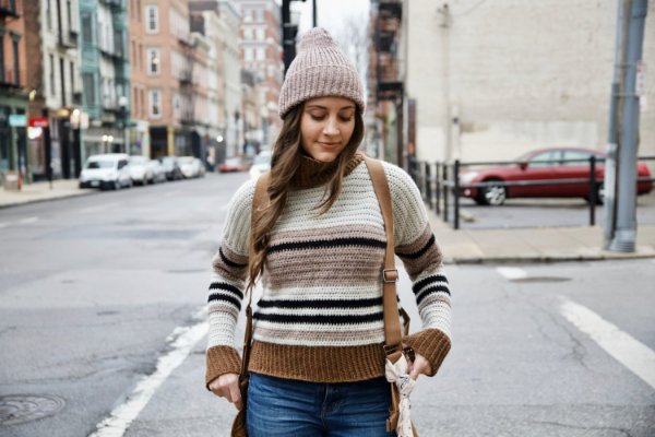 A woman wearing a beanie and a striped crochet turtleneck.