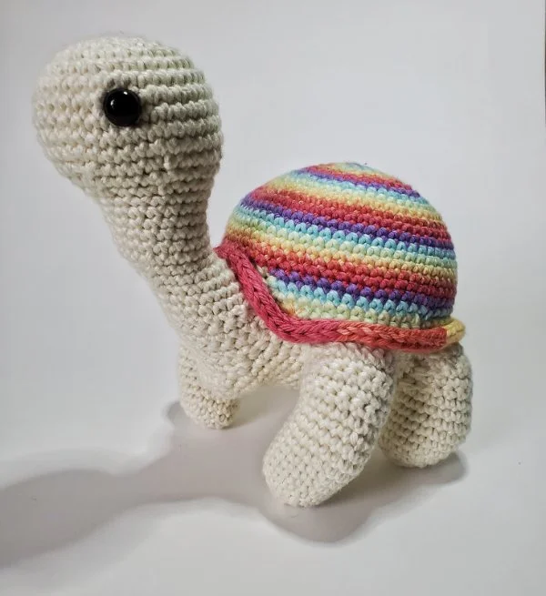 A tall crochet turtle with a long neck and a rainbow striped shell.