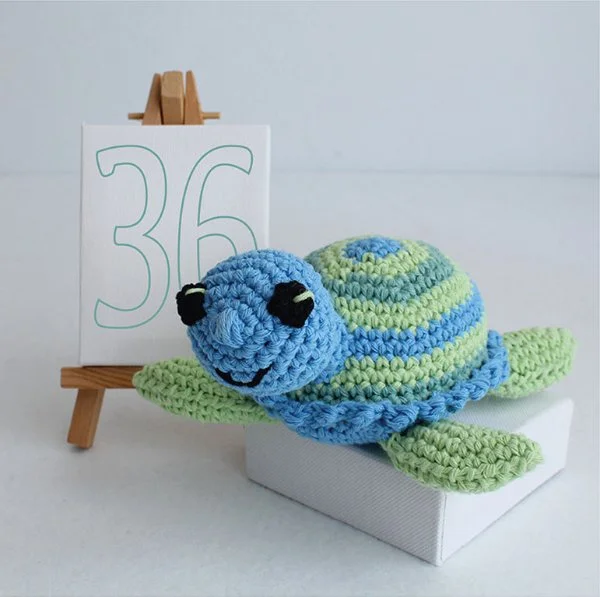 A green and blue crochet turtle with a striped shell.