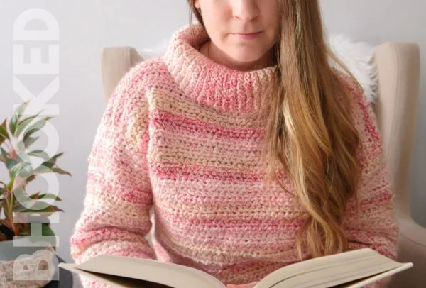 A close-up of a woman wearing a pink crochet turtleneck sweater.