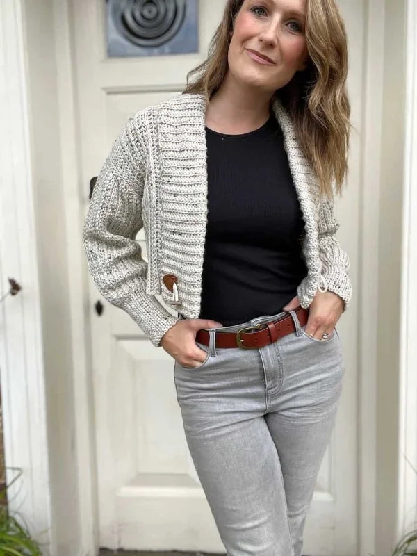 A woman wearing a grey, cropped length crochet cardigan with jeans and a black t-shirt.