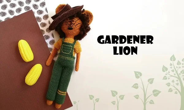 A crochet lion wearing overalls and a hat.