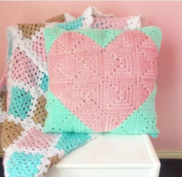 A pink and aqua crochet granny square cushion with a heart motif.
