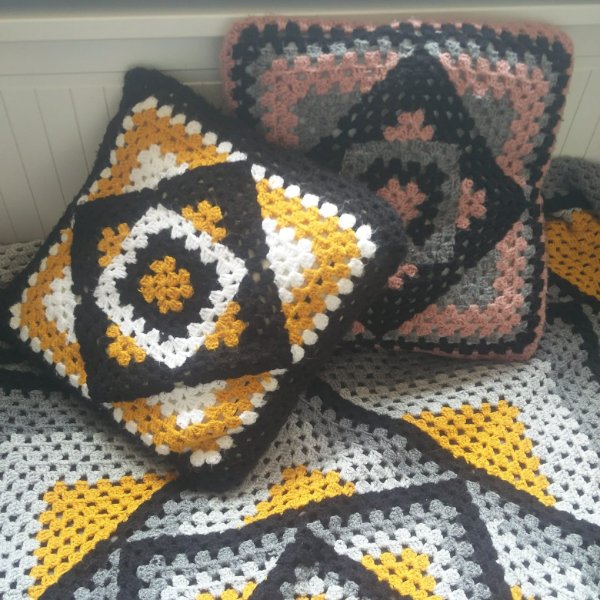 A granny square pillow with a matching blanket in shades of black, yellow, and white.