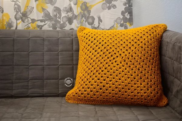 A mustard yellow granny square pillow on a grey sofa.